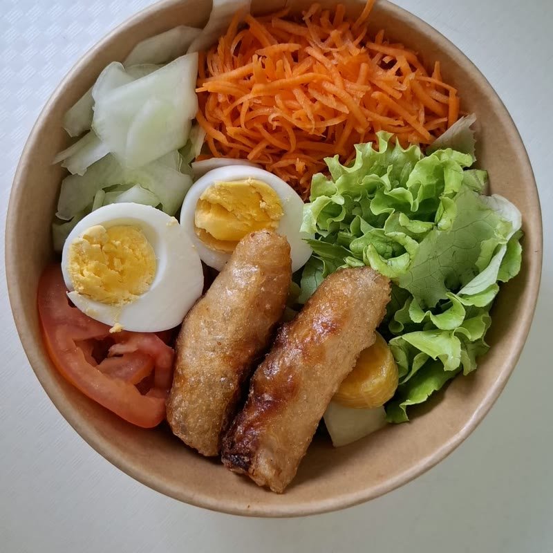 Salade composée en bol avec œuf dur, carottes râpées, salade verte et saucisses