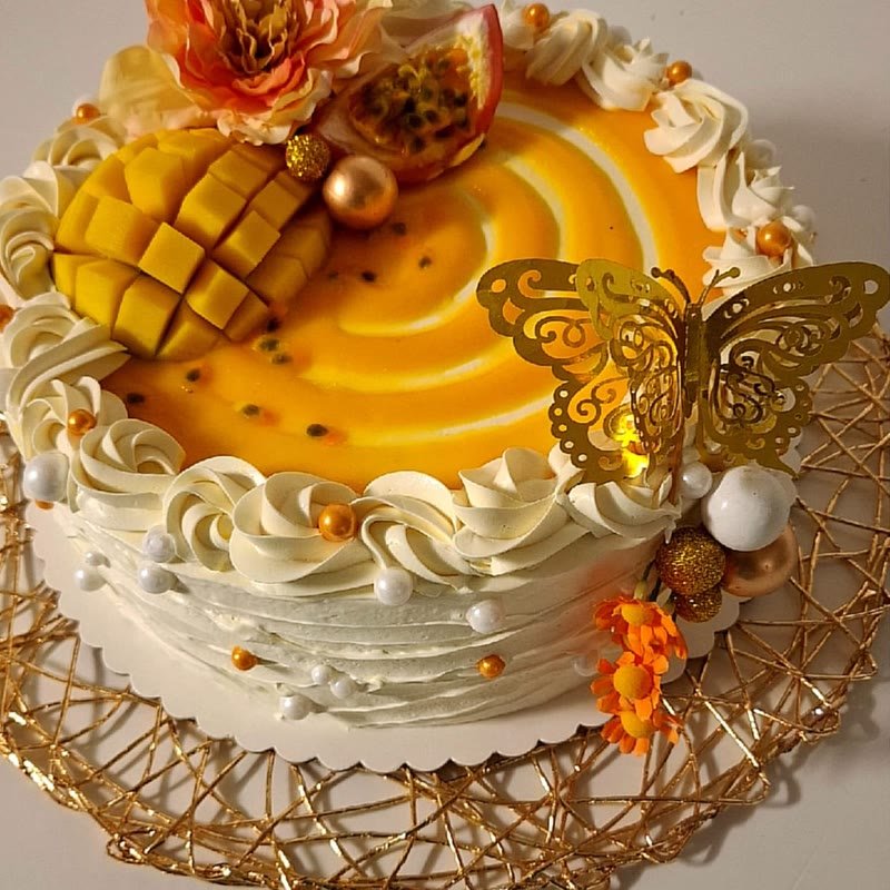 Gâteau mangue passion décoré de crème, de mangue fraîche et d'un papillon doré